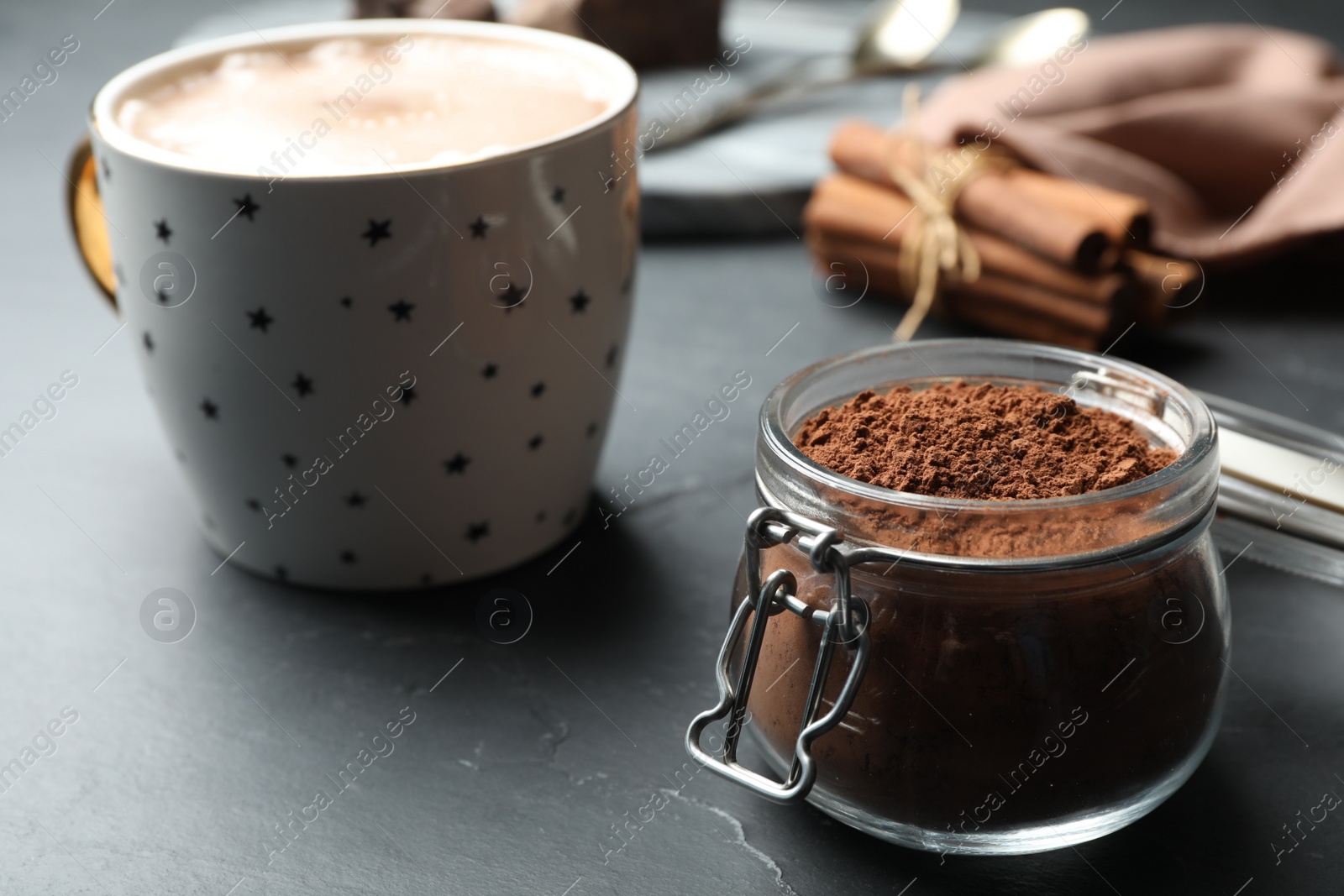Photo of Jar with cocoa powder and cup of hot drink on grey table