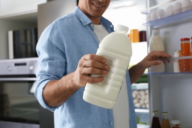 Photo of Man with gallon of milk near refrigerator in kitchen, closeup