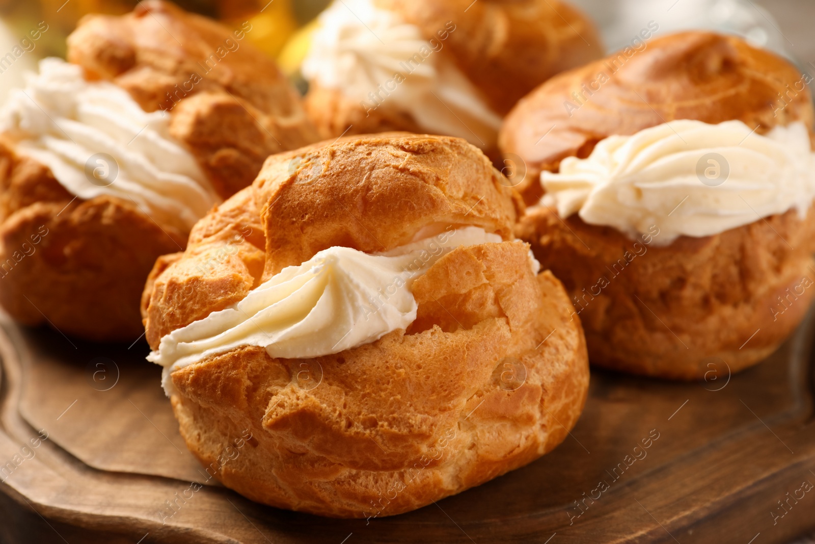 Photo of Delicious profiteroles filled with cream on wooden board, closeup