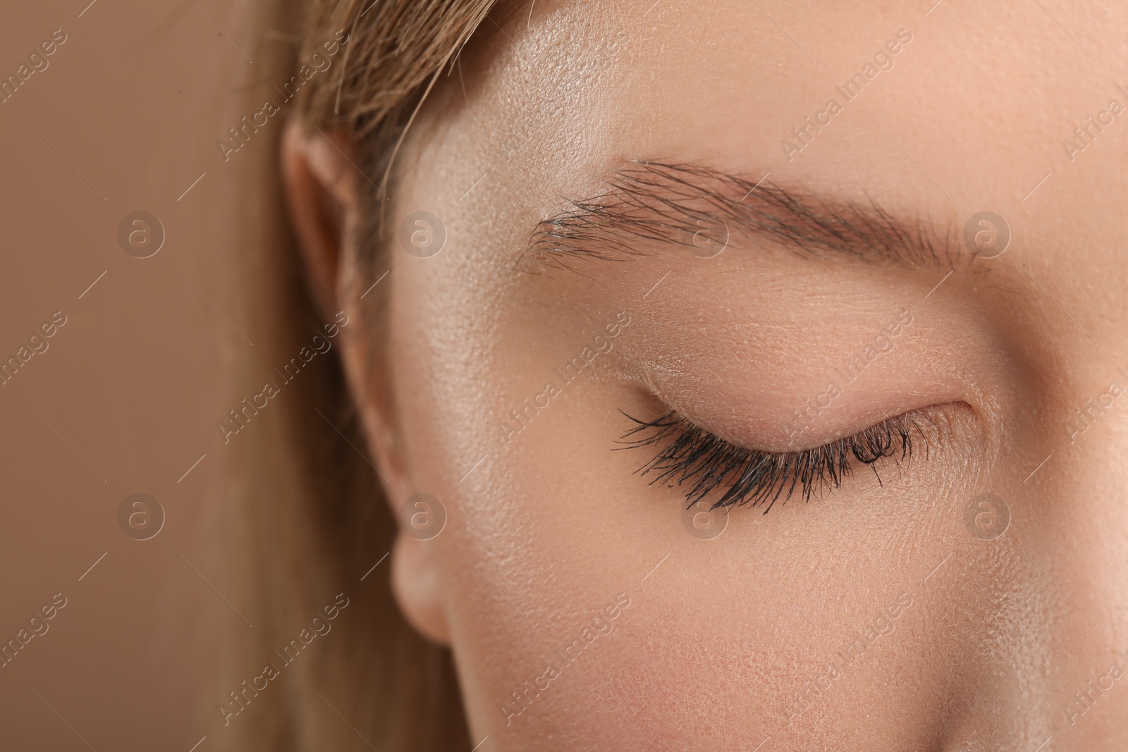 Photo of Woman with long eyelashes after mascara applying against light brown background, closeup