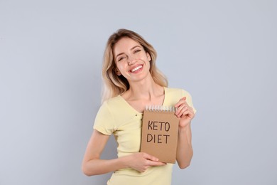Photo of Woman holding notebook with phrase Keto Diet on grey background