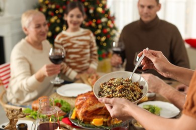 Photo of Woman with bowl of traditional Christmas kutia and her family at festive dinner, focus on hands. Slavic dish