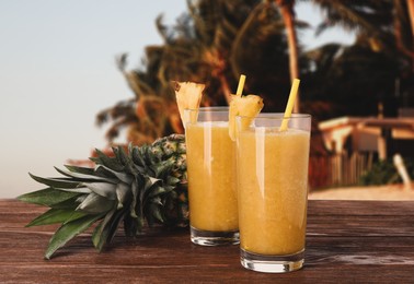 Image of Tasty pineapple smoothie in glasses on wooden table against blurred background