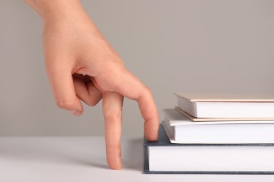 Photo of Woman imitating stepping up on books with her fingers against grey background, closeup