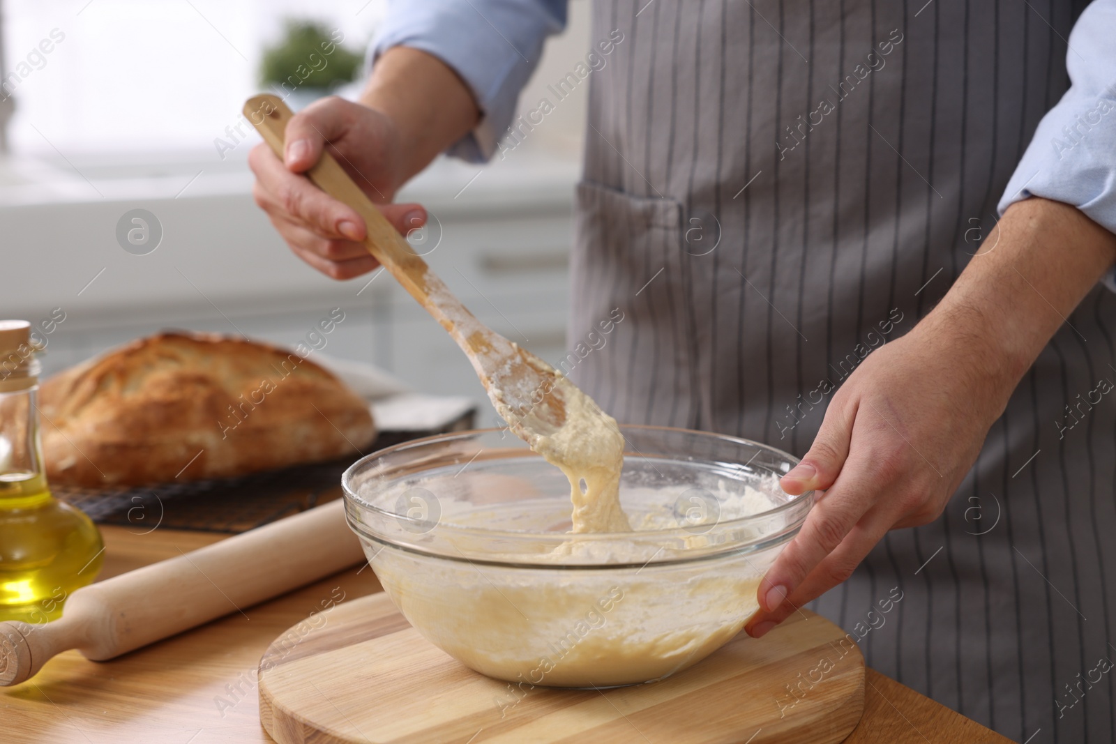 Photo of Making bread. Man preparing dough at wooden table in kitchen, closeup