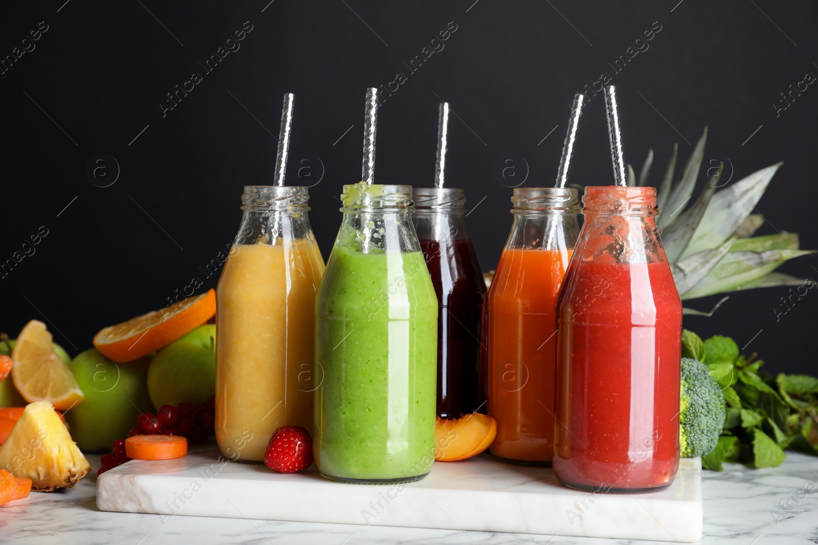 Photo of Bottles of delicious juices and fresh fruits on white marble table