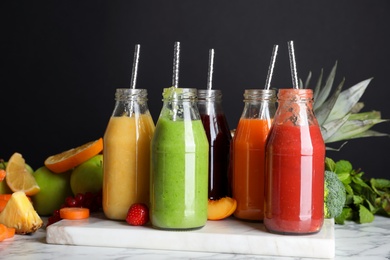 Bottles of delicious juices and fresh fruits on white marble table