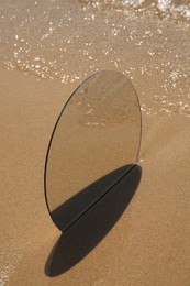 Photo of Round mirror reflecting sea on sandy beach