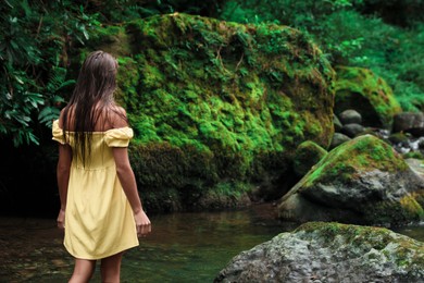 Beautiful young woman in dress near mountain river outdoors, back view. Space for text