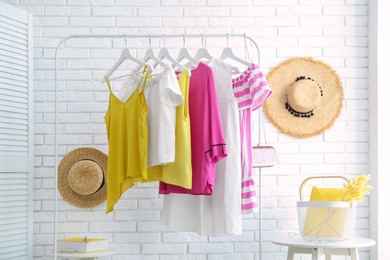 Photo of Wardrobe rack with women's clothes at white brick wall in room