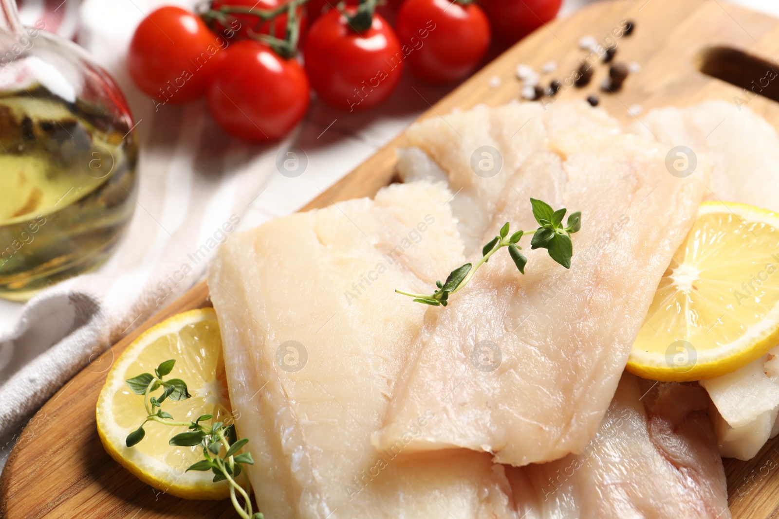 Photo of Pieces of raw cod fish, lemon, tomatoes and oil on table, closeup