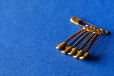 Photo of Golden safety pins on blue background, closeup. Space for text