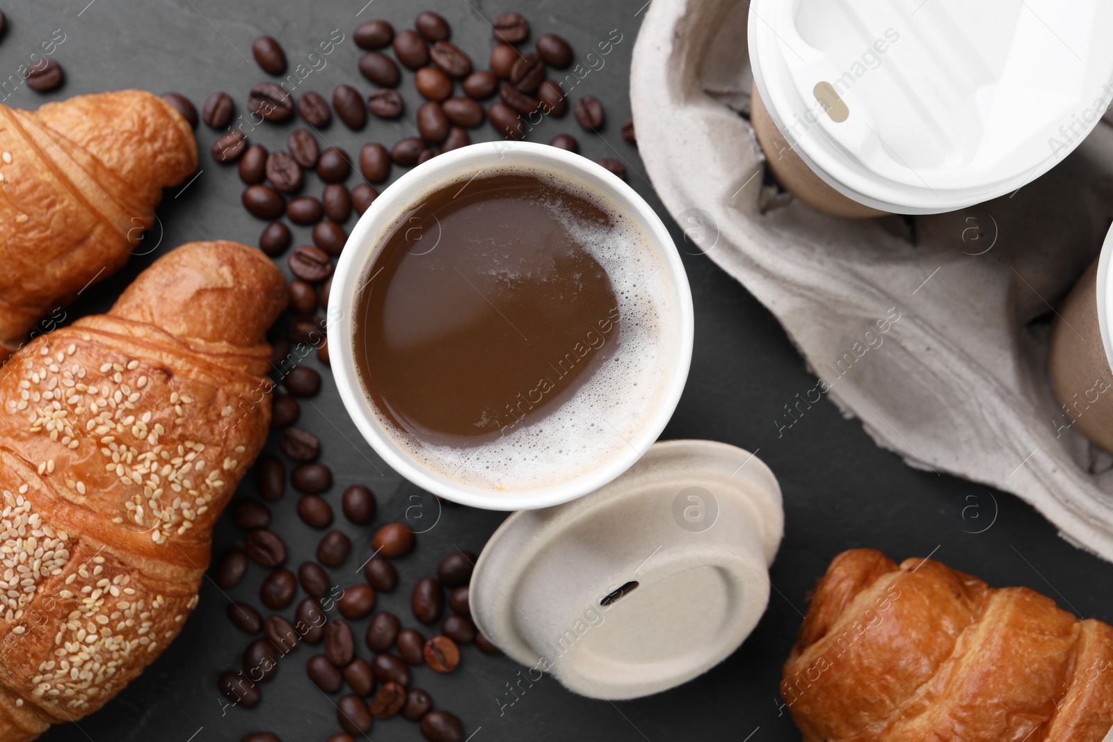 Photo of Coffee to go. Paper cups with tasty drink, croissants and beans on black table, flat lay