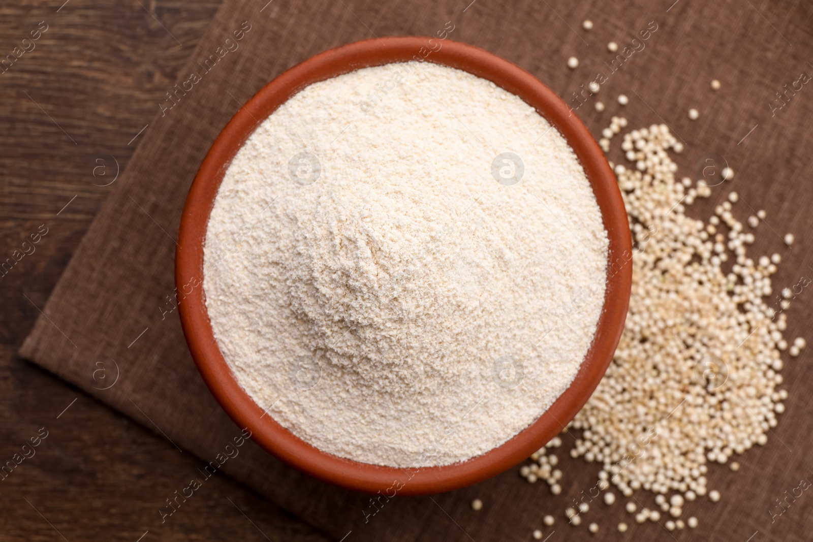 Photo of Quinoa flour in bowl and seeds on wooden table, top view