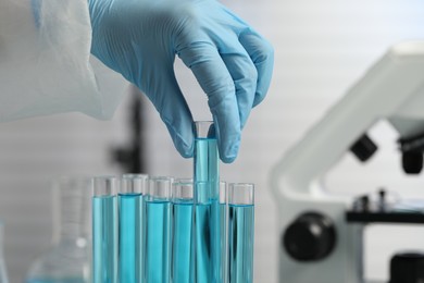 Photo of Scientist taking test tube with light blue liquid in laboratory, closeup