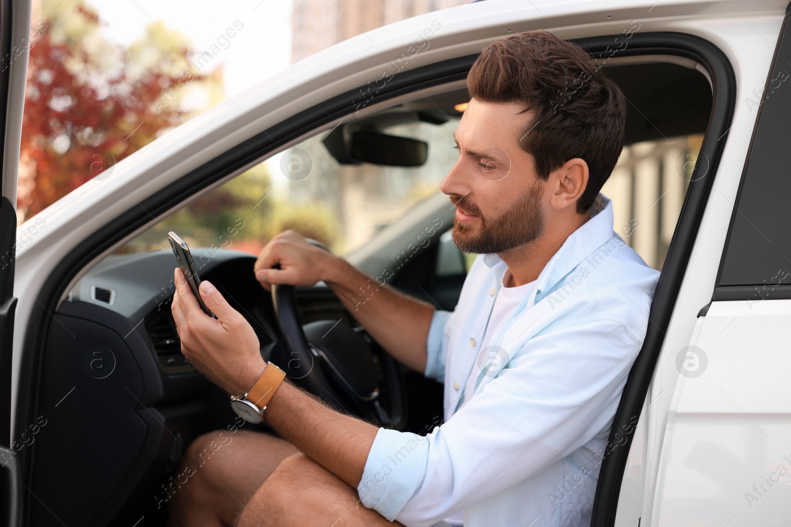 Photo of Happy bearded man with smartphone sitting in car