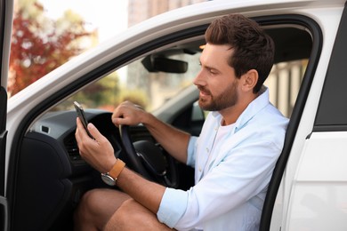 Happy bearded man with smartphone sitting in car