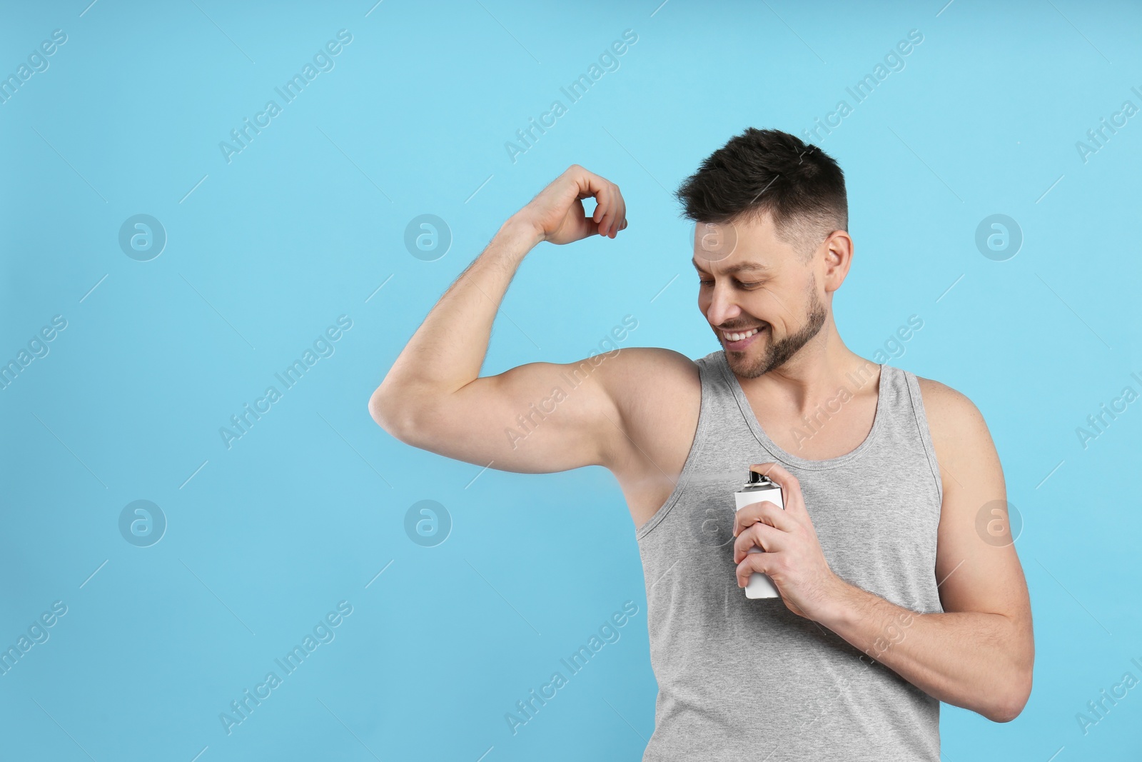 Photo of Handsome man applying deodorant on turquoise background. Space for text