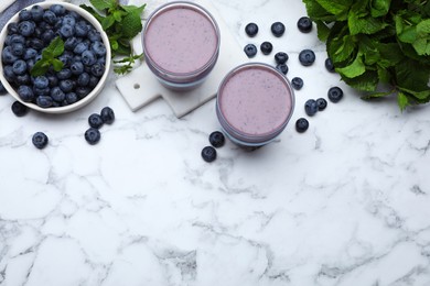 Glasses of blueberry smoothie with mint and fresh berries on white marble table, flat lay. Space for text