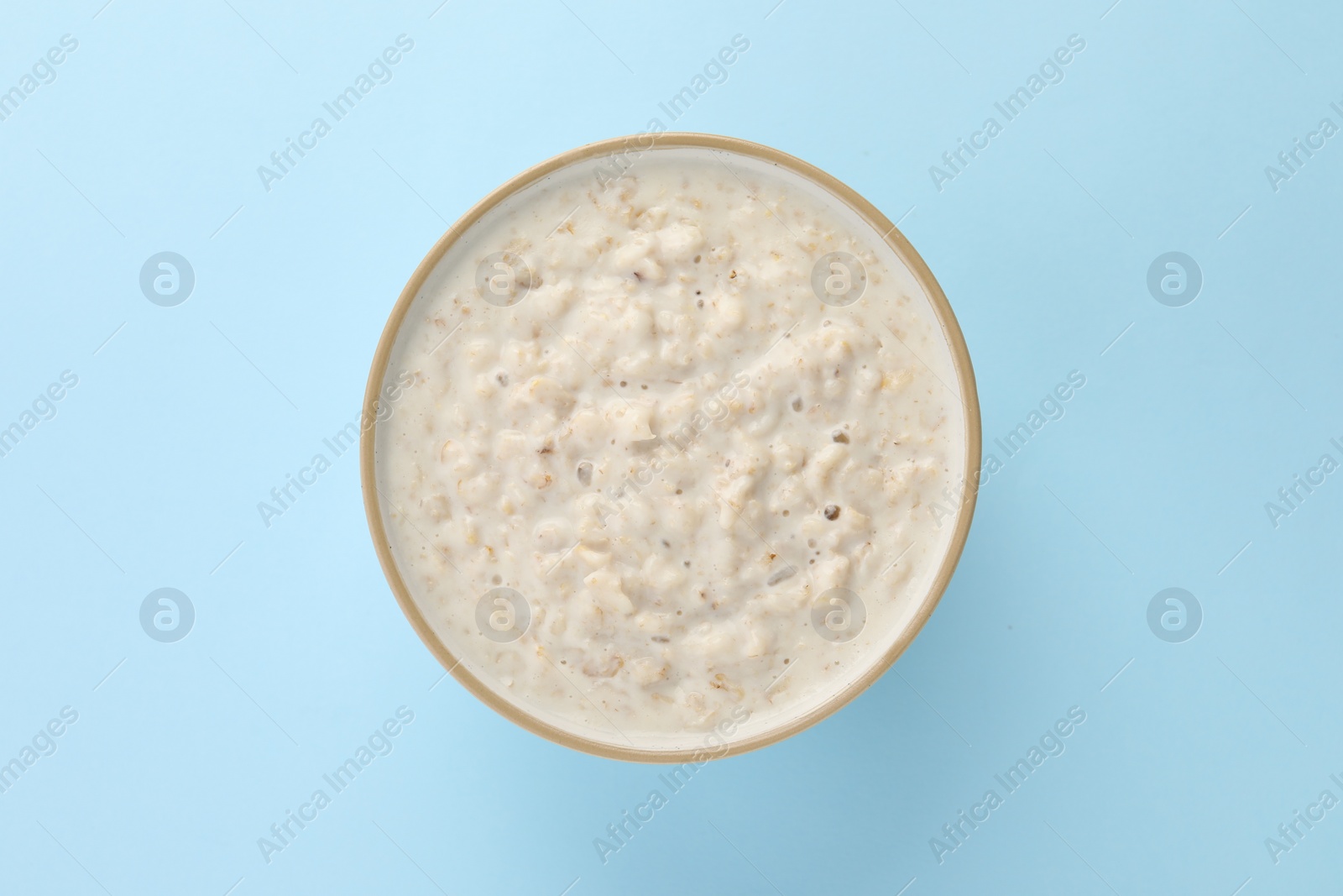 Photo of Tasty boiled oatmeal in bowl on light blue table, top view