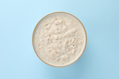 Tasty boiled oatmeal in bowl on light blue table, top view