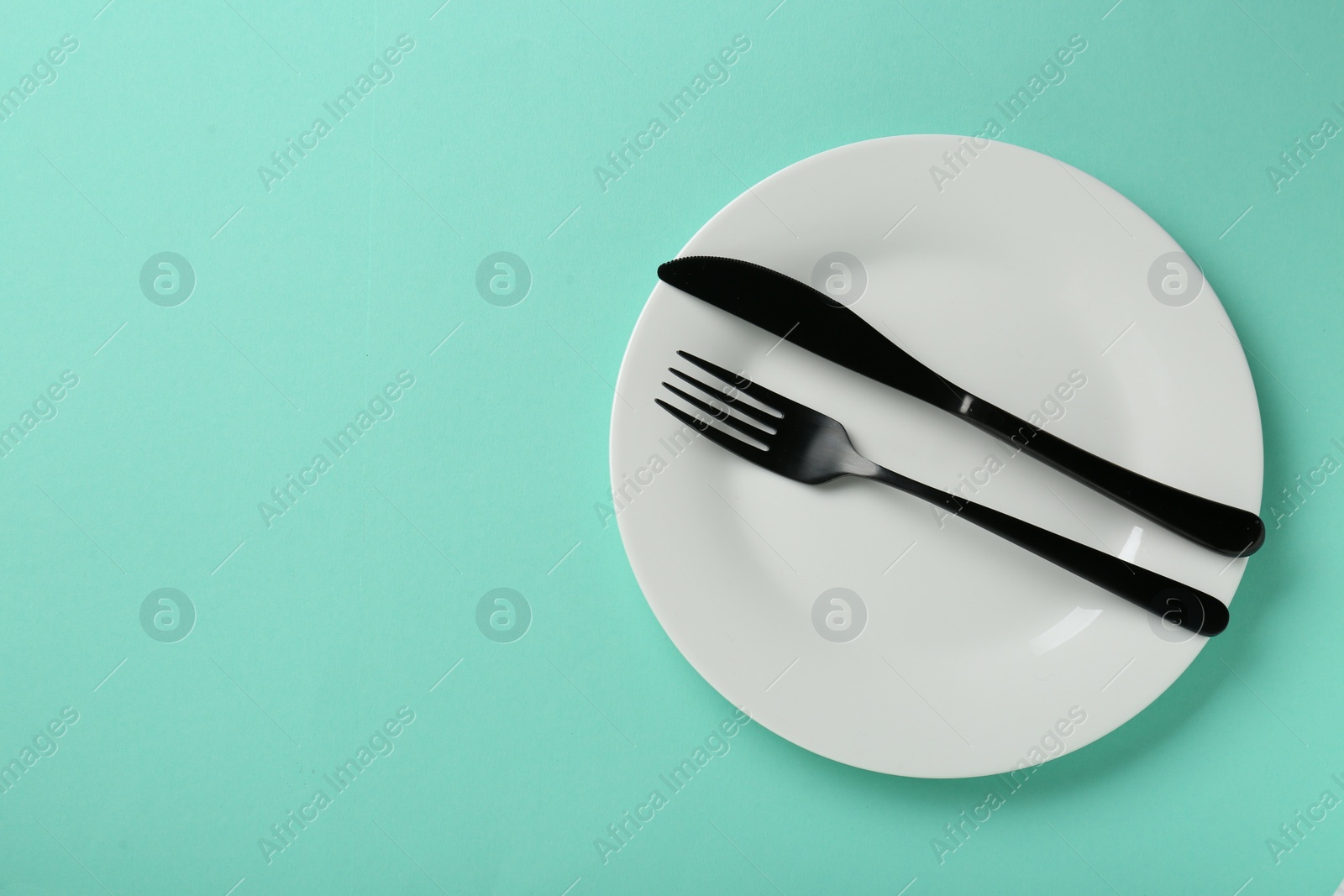 Photo of Clean white plate with cutlery on turquoise background, top view. Space for text