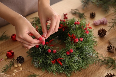 Photo of Florist making beautiful Christmas wreath with berries at wooden table indoors, closeup