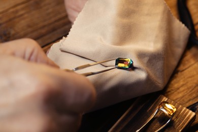 Professional jeweler working with gemstone at wooden table, closeup