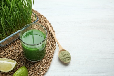 Photo of Composition with glass of wheat grass juice and lime on white wooden table. Space for text