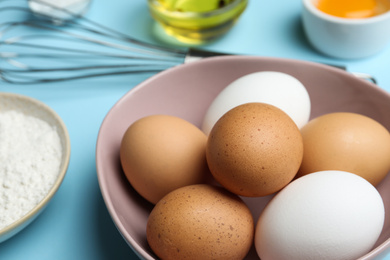 Photo of Raw eggs in bowl on light blue background, closeup