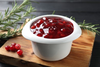 Photo of Cranberry sauce in bowl, fresh berries and rosemary on table, closeup