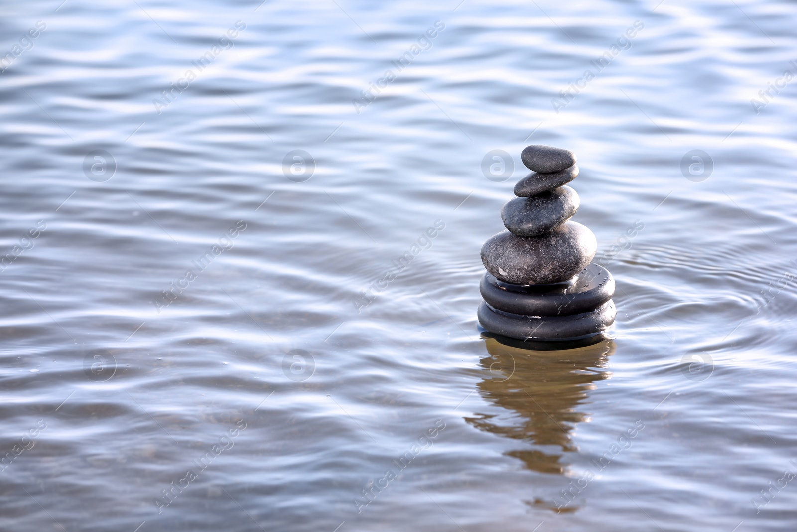 Photo of Stack of dark stones in sea water, space for text. Zen concept