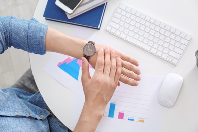 Photo of Young businessman checking time on his wristwatch at workplace, top view. Time management