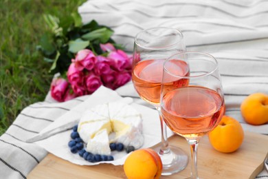 Glasses of delicious rose wine, flowers and food on picnic blanket outdoors