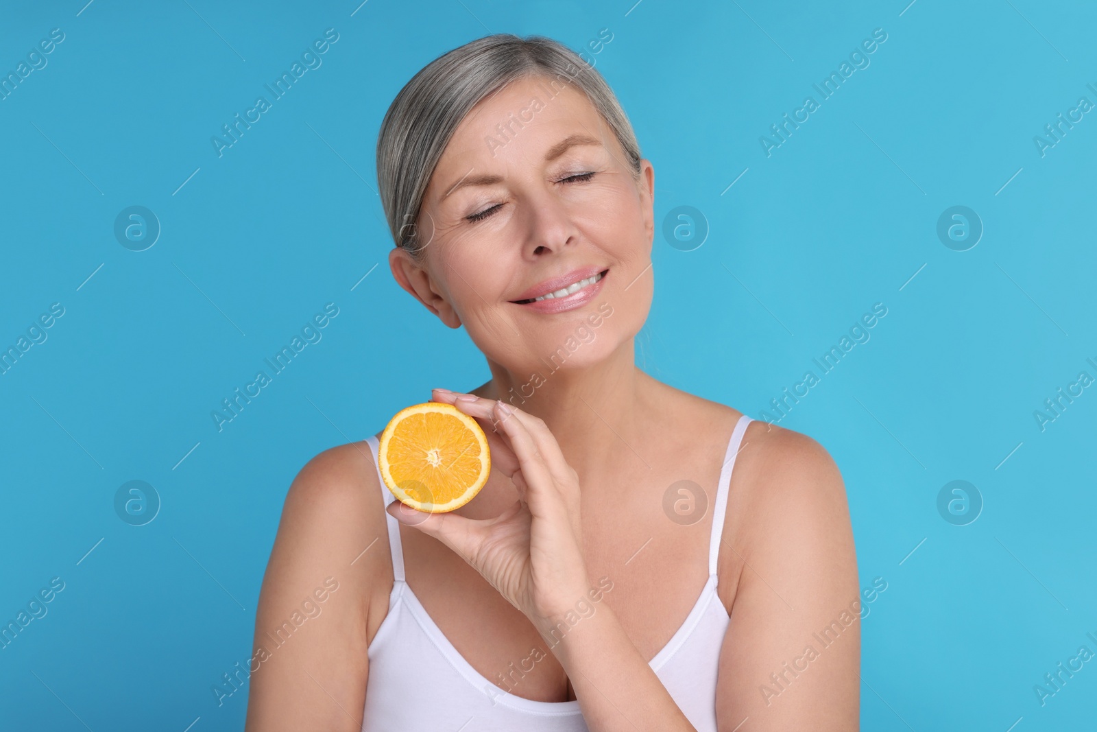 Photo of Beautiful woman with half of orange rich in vitamin C on light blue background