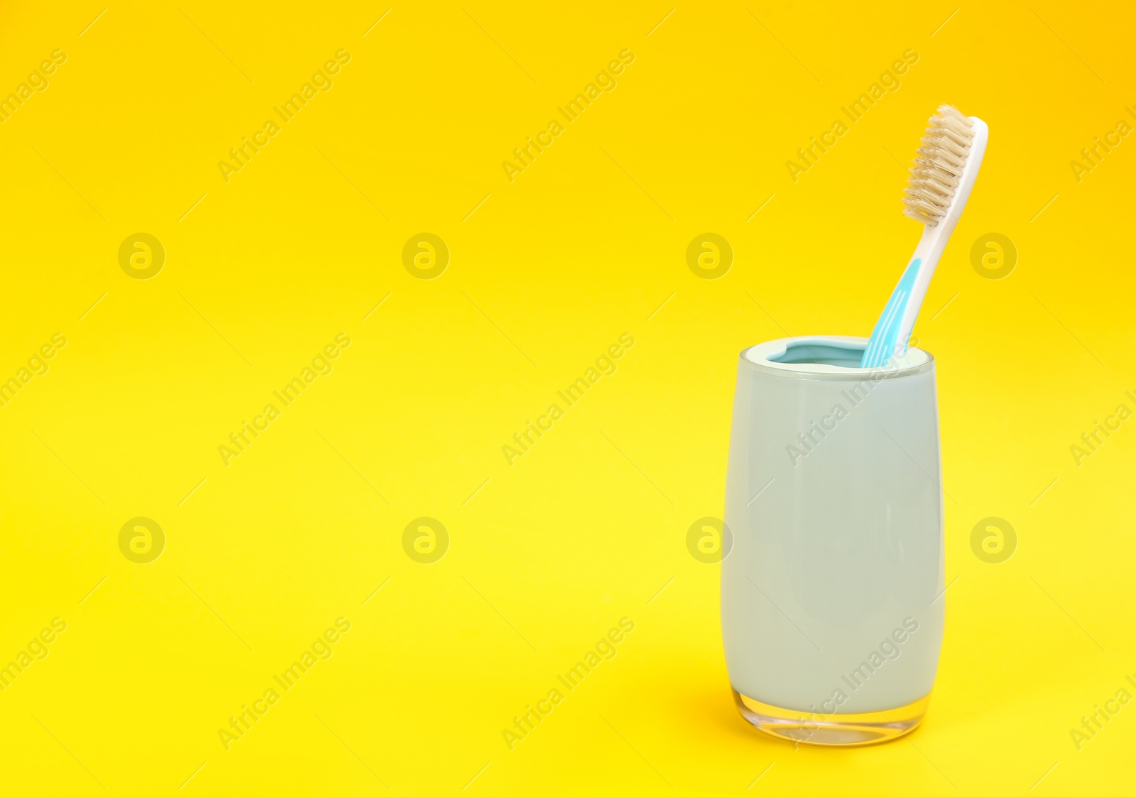 Photo of Natural bristle toothbrush in holder on yellow background. Space for text