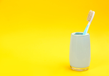 Photo of Natural bristle toothbrush in holder on yellow background. Space for text