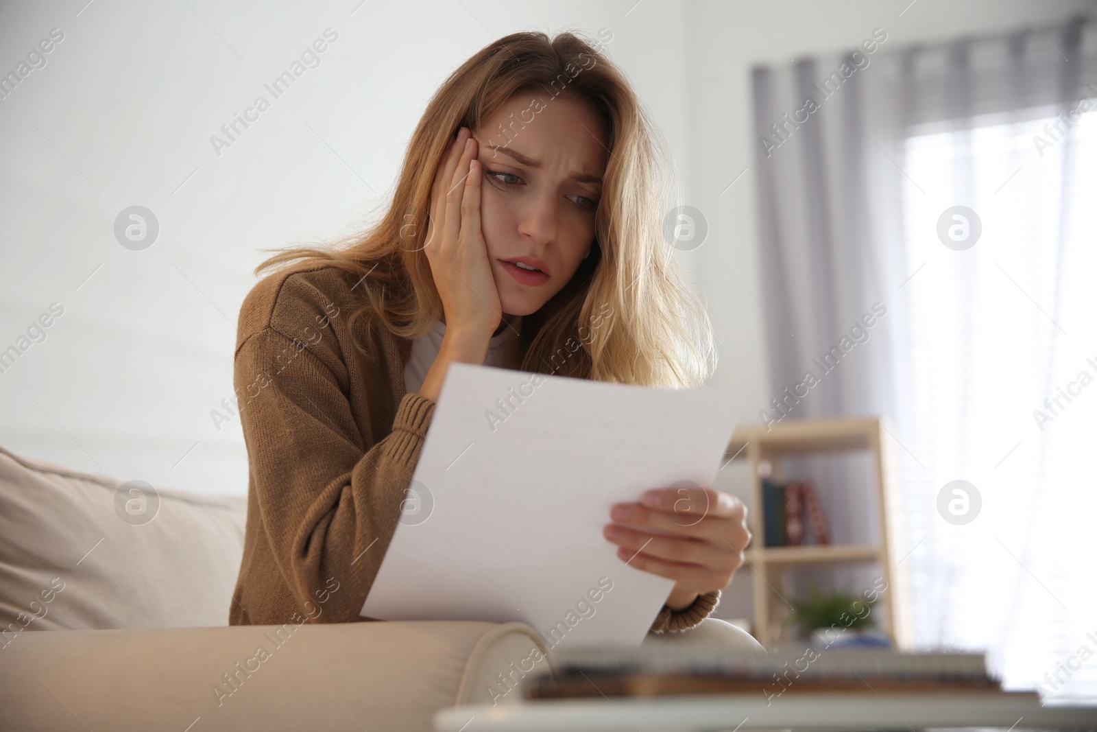 Photo of Worried woman reading letter on sofa at home