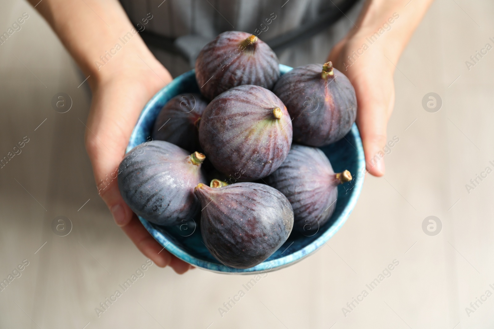 Photo of Woman holding bowl with fresh ripe figs on light background, top view