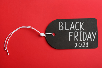 Photo of Tag with words BLACK FRIDAY 2021 on red background, top view
