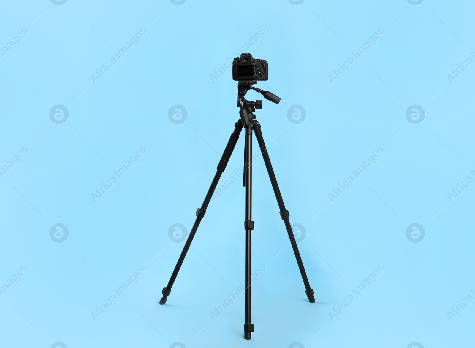 Photo of Modern tripod with professional camera on light blue background