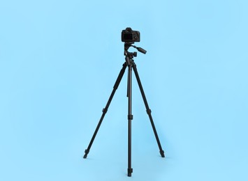 Modern tripod with professional camera on light blue background