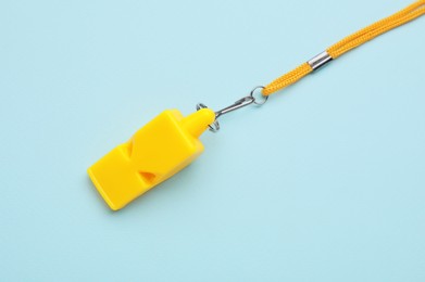 One yellow whistle with cord on light blue background, top view