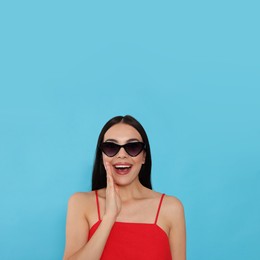 Photo of Attractive happy woman in fashionable sunglasses against light blue background
