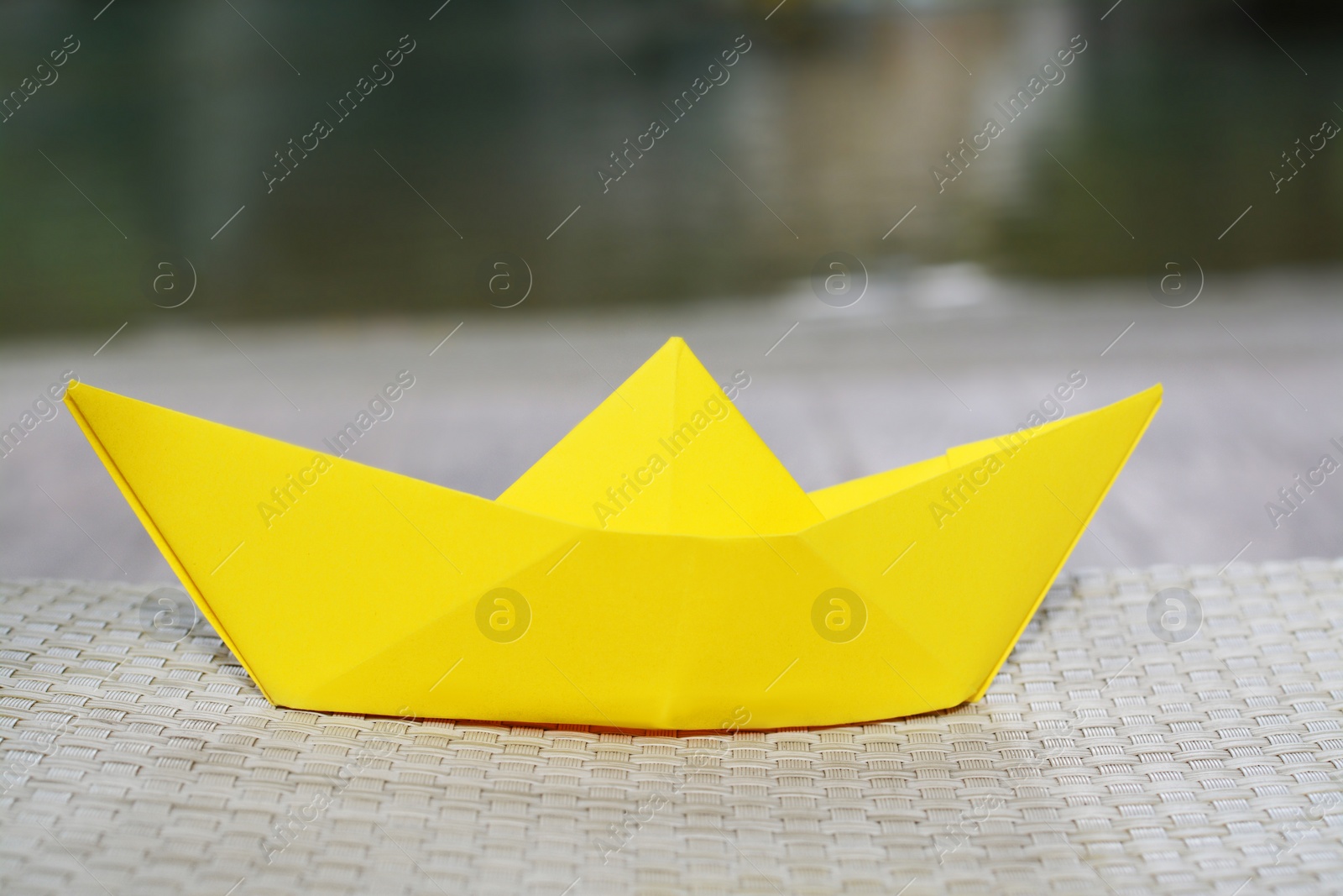 Photo of Beautiful yellow paper boat on wicker sunbed, closeup