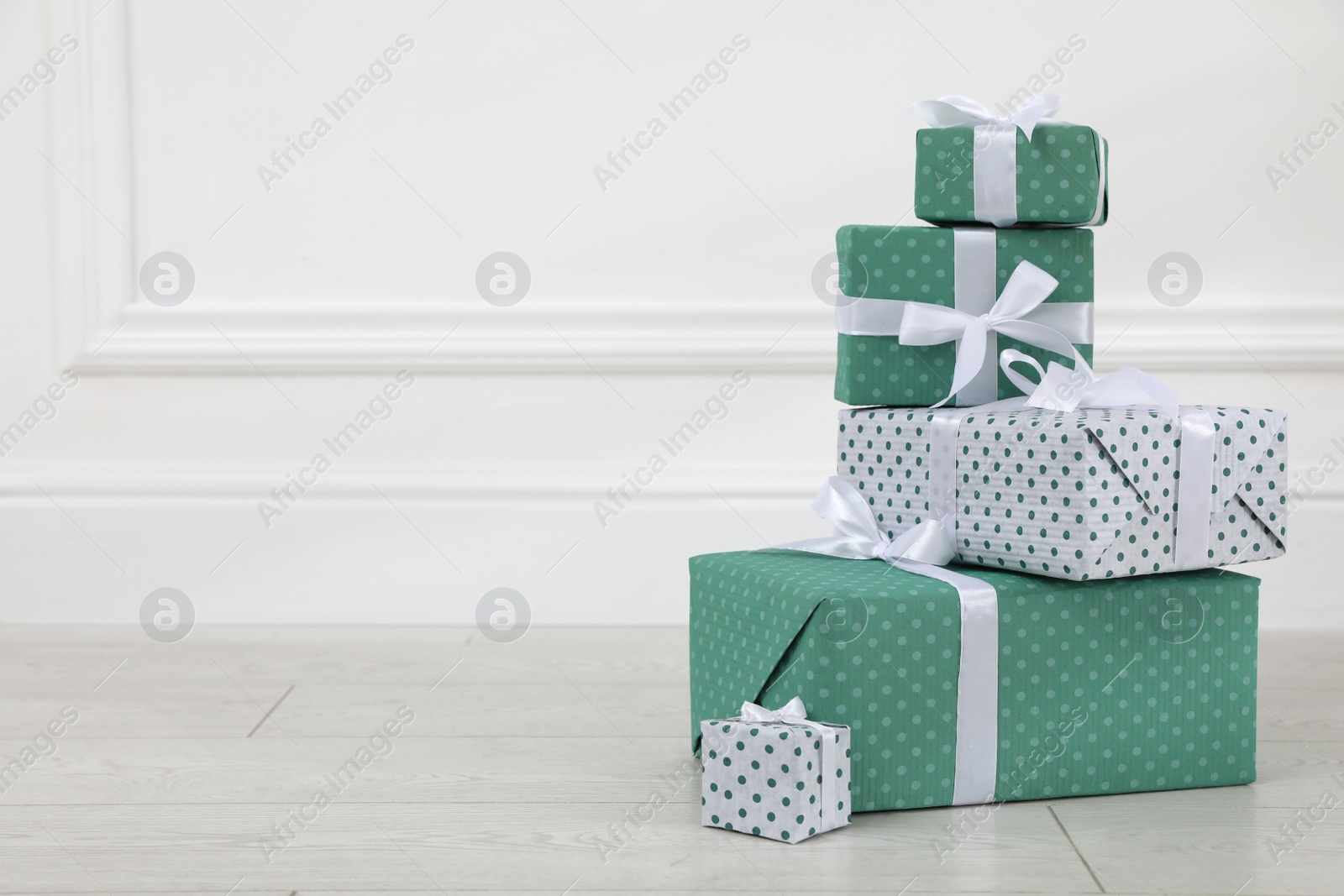 Photo of Many gift boxes on wooden floor near white wall. Space for text