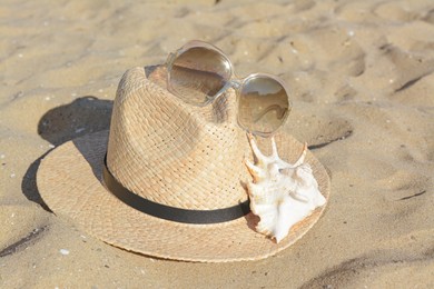 Photo of Stylish straw hat, sunglasses and sea shell on sandy beach