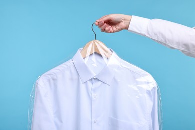 Photo of Dry-cleaning service. Woman holding shirt in plastic bag on light blue background, closeup