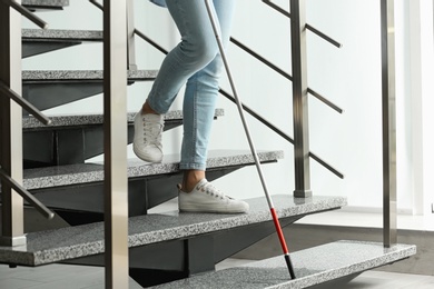 Photo of Blind person with long cane going down stairs indoors, closeup