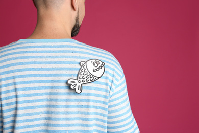 Photo of Man with paper fish on back against pink background, closeup. April fool's day